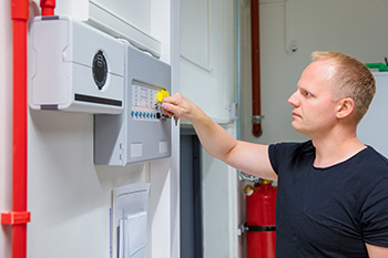 Tech in a blue shirt performing NJ fire alarm service on a panel